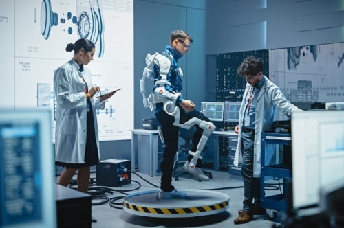 In Robotics Development Laboratory: Engineers and Scientists Work on a Bionics Exoskeleton Prototype with Person Testing it. Designing Wearable Exosuit to Help Disabled People, Warehouse Workers